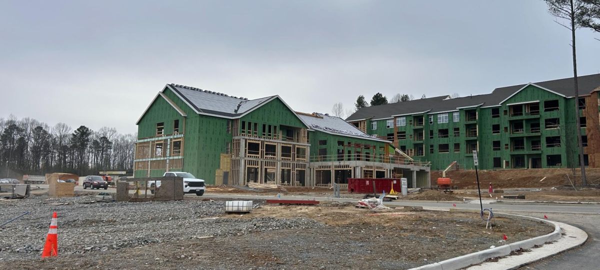 Developing apartment complex with partially completed buildings and roadway in foreground surrounded by trees