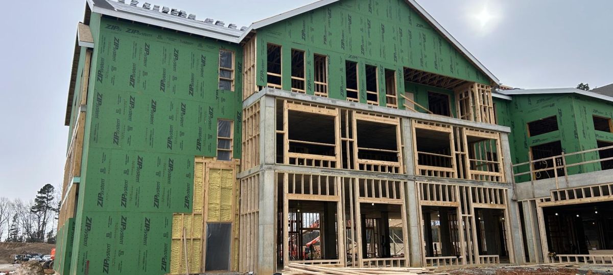 Close-up of apartment building under construction showing wooden framing, concrete base, and green exterior sheathing