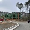 Apartment buildings nearing completion next to wooded area with dirt path and construction equipment.