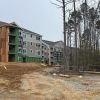 Construction site with multi-story apartment buildings framed in green sheathing and exposed wood structure under overcast sky.